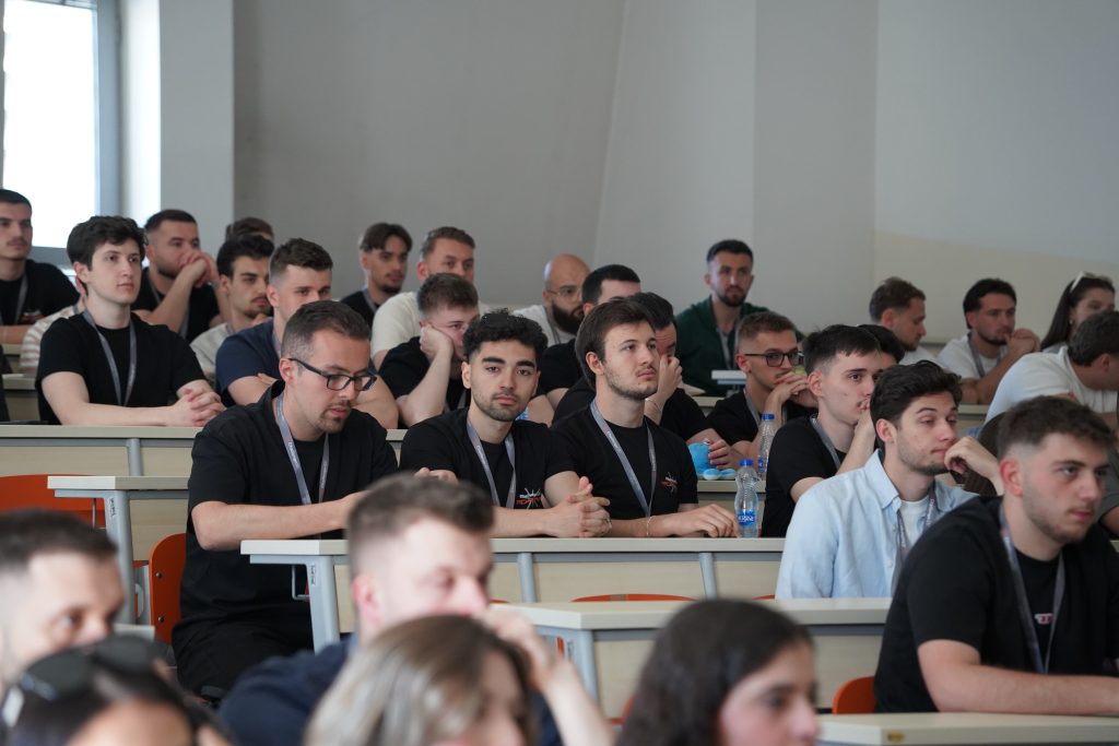 Hackathon participants sit in a lecture hall and listen to a presentation.
