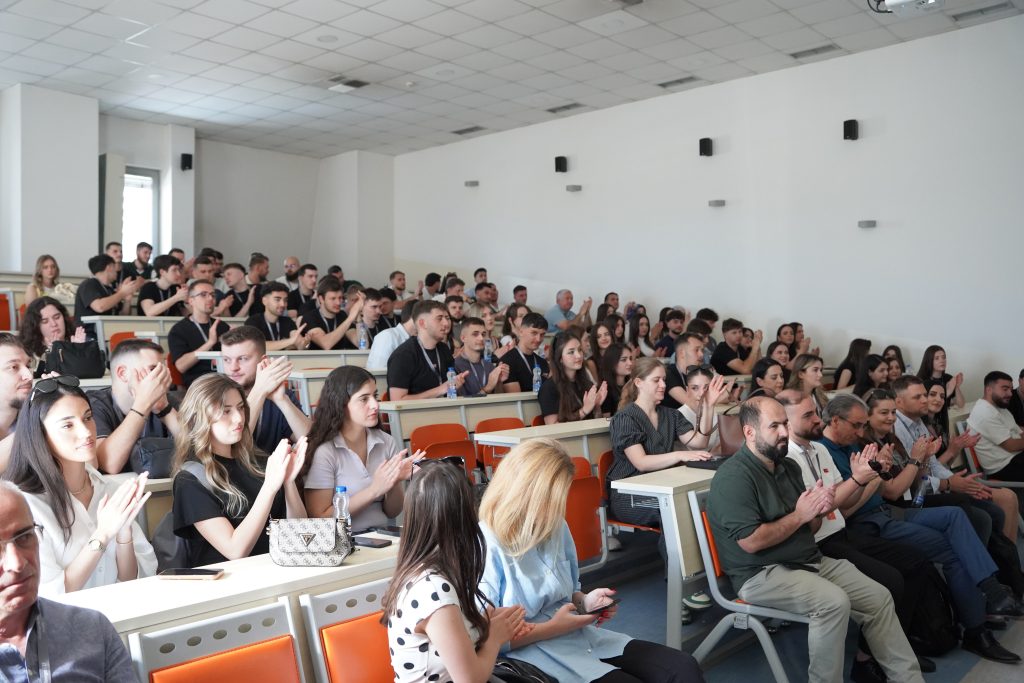 A lecture hall filled with hackathon participants applauding after a presentation.
