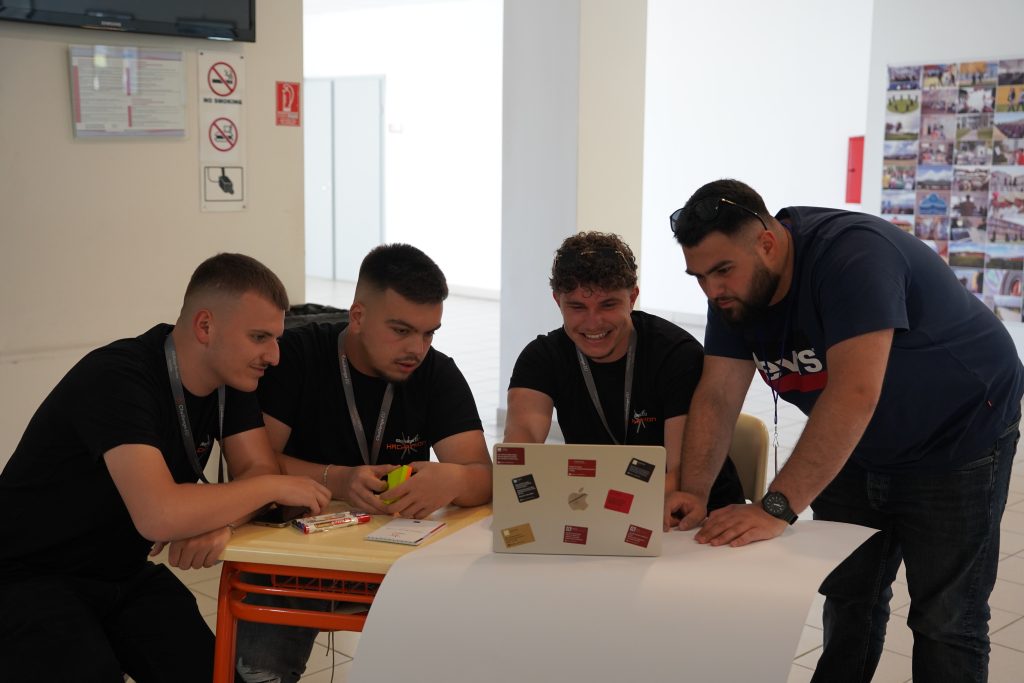 A four-person team of hackathon participants works together on a project using a laptop.