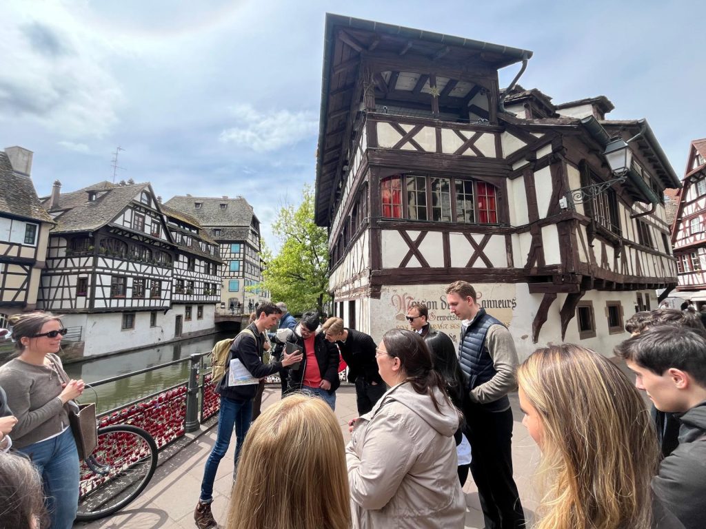 Students gather for a guided tour in a historic district with half-timbered buildings.