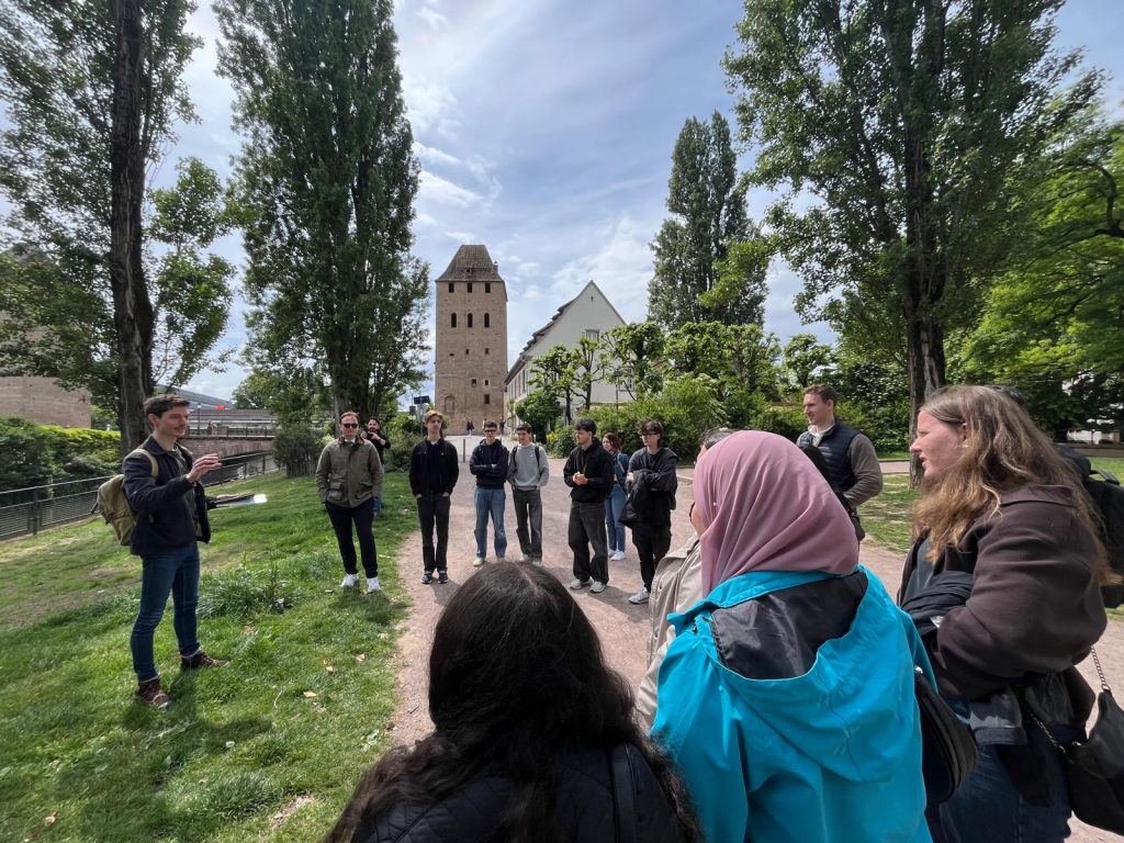 A group of students listens to a guide during an outdoor city tour near a historic tower.