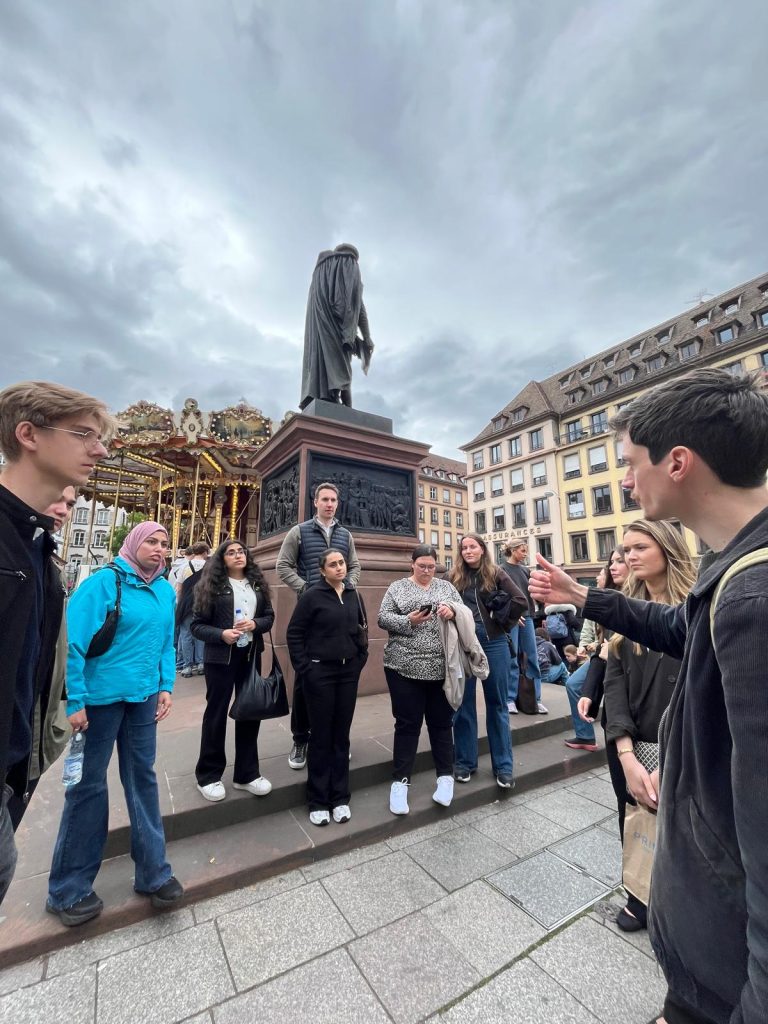 A group of students takes part in a guided city walk near a monument and carousel.