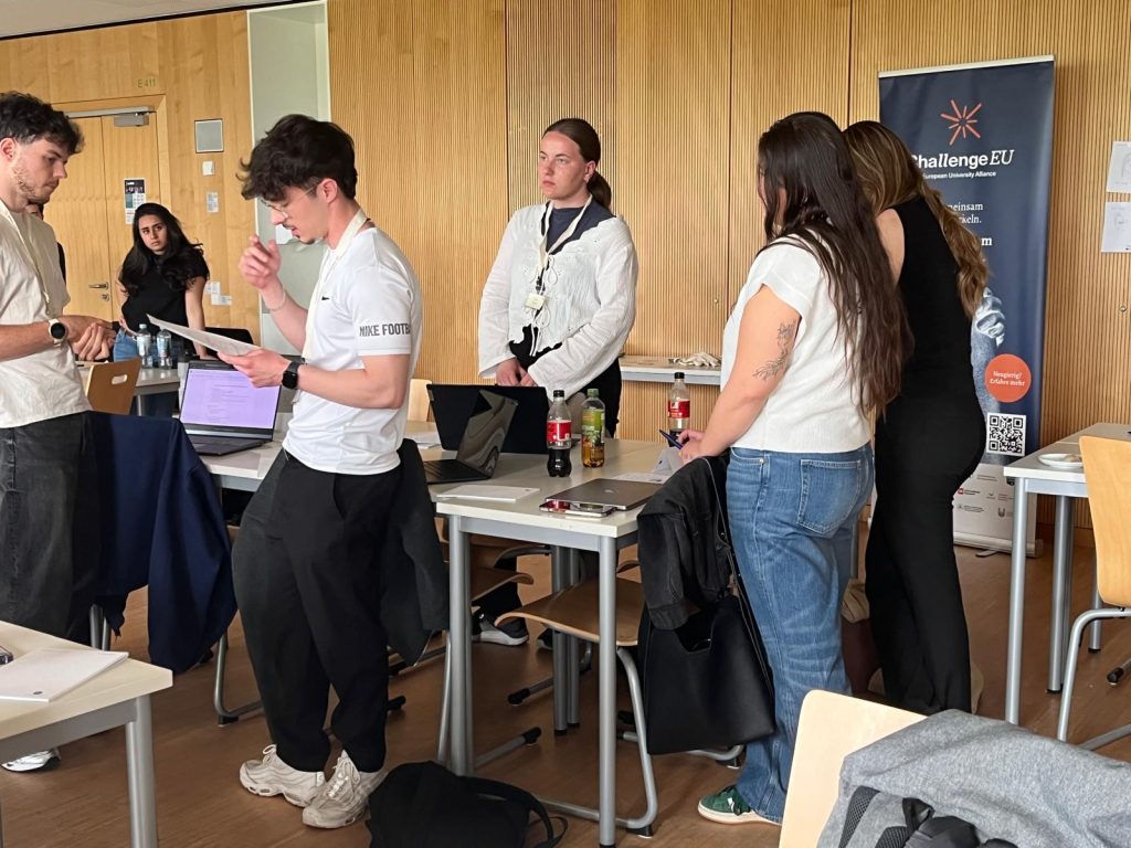 Students stand in small groups during an interactive workshop session, with a ChallengeEU banner in the background.