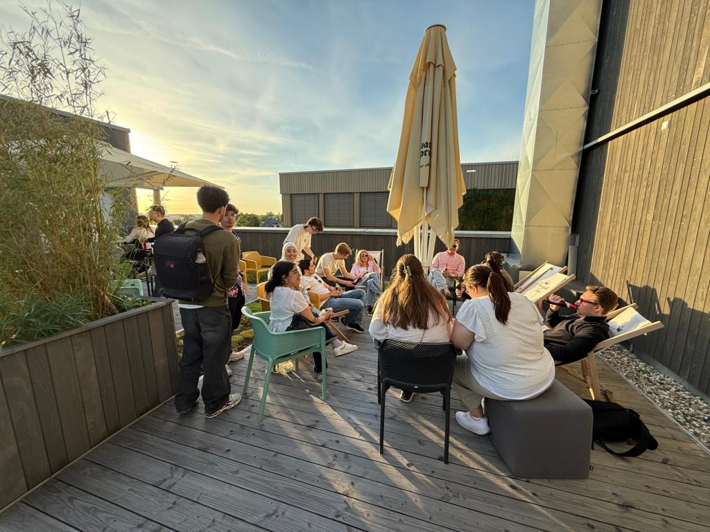 Students sit together on an outdoor terrace at sunset during an informal gathering.