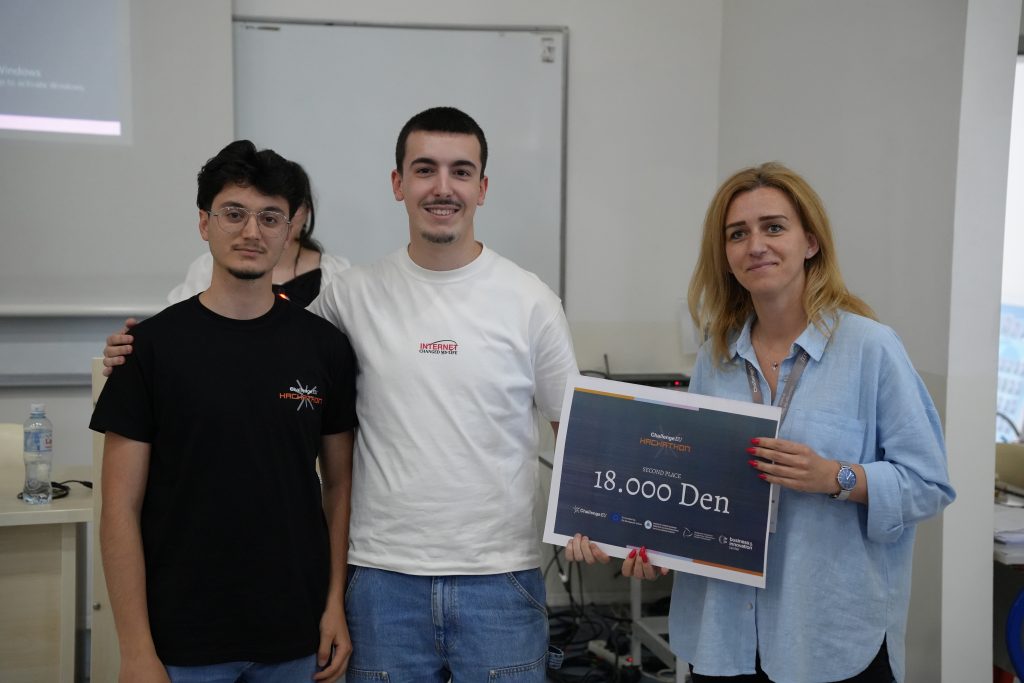 Two student participants and an organiser pose with a second-place award certificate for 18,000 denars during the ChallengeEU Hackathon.