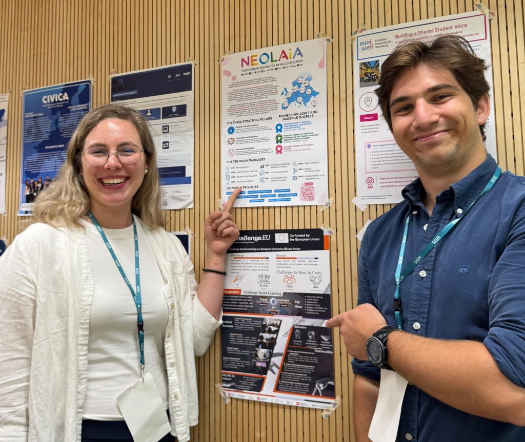 Two student representatives point to the ChallengeEU poster displayed among other European University Alliance posters.