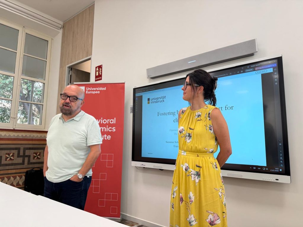 Two lecturers standing beside a screen displaying a presentation on encouraging behavioural support for climate action.