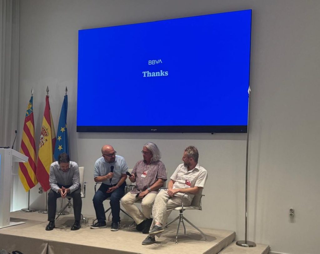 Four speakers seated on stage during a roundtable discussion, with a BBVA presentation displayed behind them.